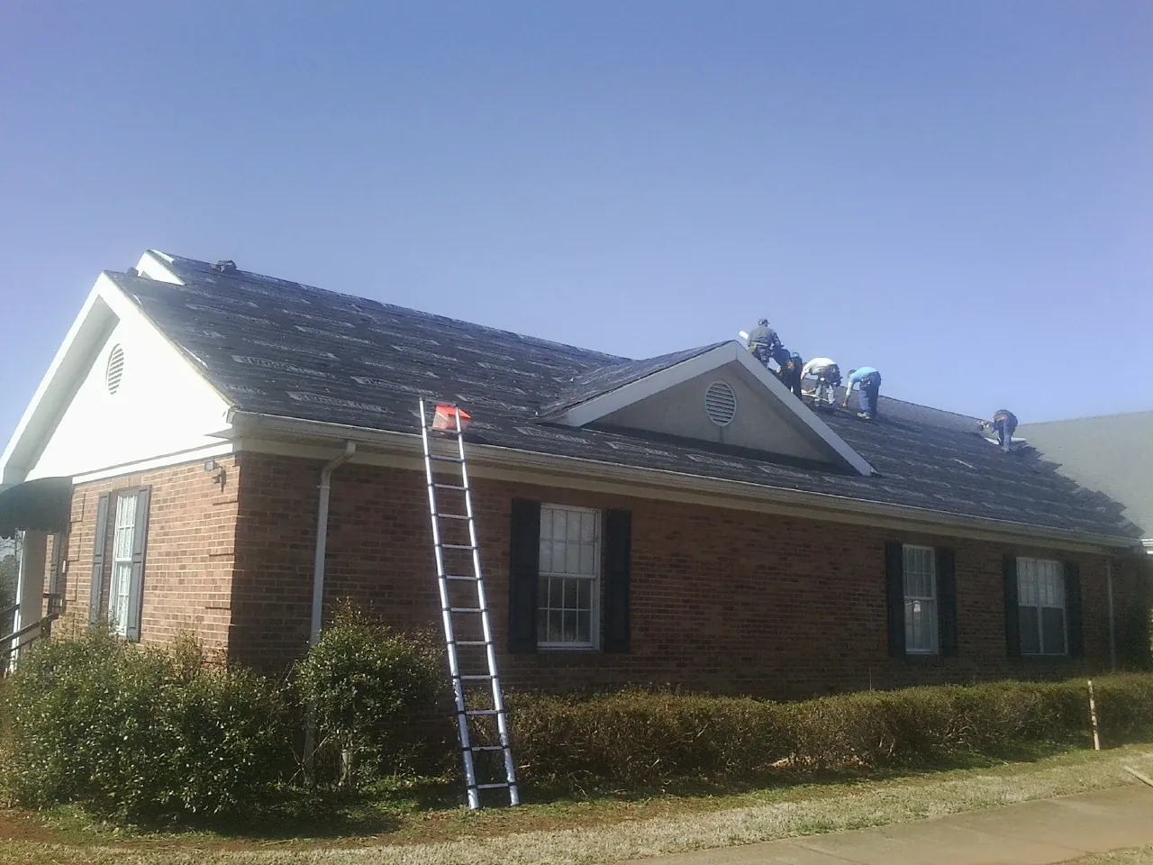Crew tearing shingles off a brick ranch roof with a ladder set — Emergency Roof Repair work by our crew in Mountain View