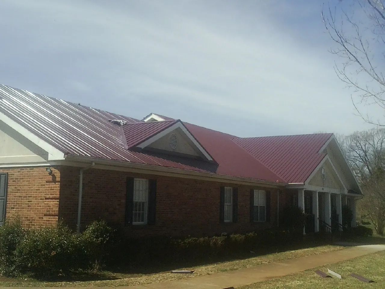 Red metal roof with gabled entries on a long brick building, from a Hail Damage Roof Repair job in Mountain View