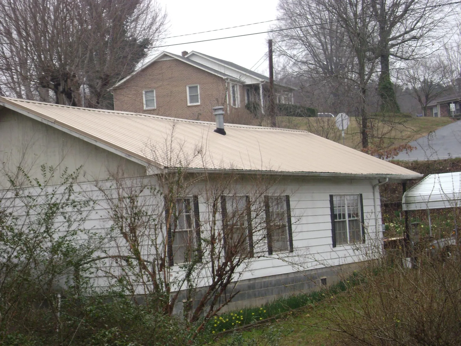 Tan metal roof on a white sided house set into a hillside — Commercial Roofing by Roofing Brothers in Mountain View